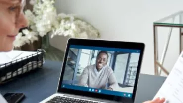 Woman holding a resume during a video call with a man on a laptop.