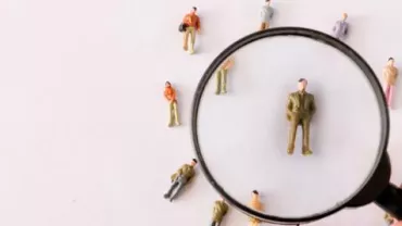 Magnifying glass over mini figures, focusing on one person.