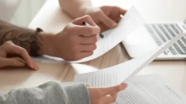 Two people reviewing documents with a laptop on a wooden desk