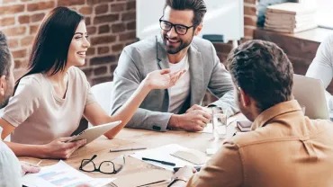 Team having a lively discussion around a wooden table in a modern office.