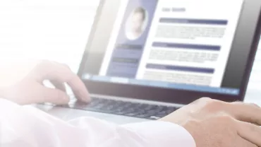 Person reviewing a resume on a laptop screen, hands resting on the keyboard.