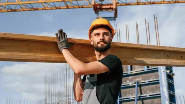 a construction worker with a hard hat lifting a blank of wood