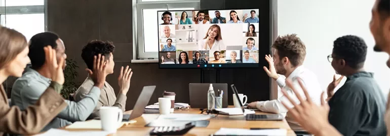 Team in a conference room participating in a video call with people displayed on a large screen.
