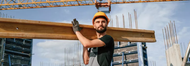 a construction worker with a hard hat lifting a blank of wood